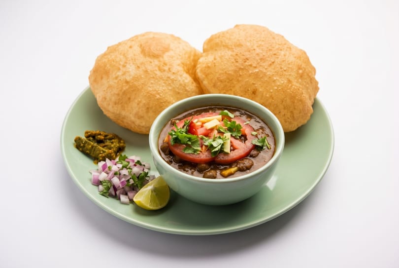 Chole Bhature, a popular Indian dish, with two fried breads, chickpea curry, and sides on a green plate.