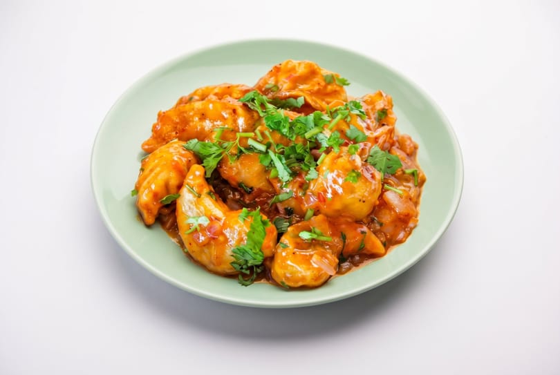 Chili momos, a popular Indo-Chinese dish, served on a light green plate with cilantro garnish.