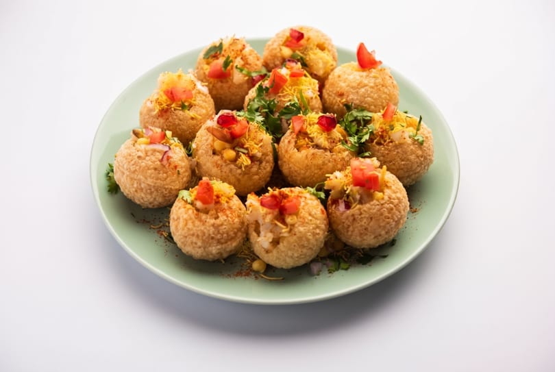 A plate of crispy pani puri, filled with potatoes, chickpeas, spices, and topped with tomatoes.